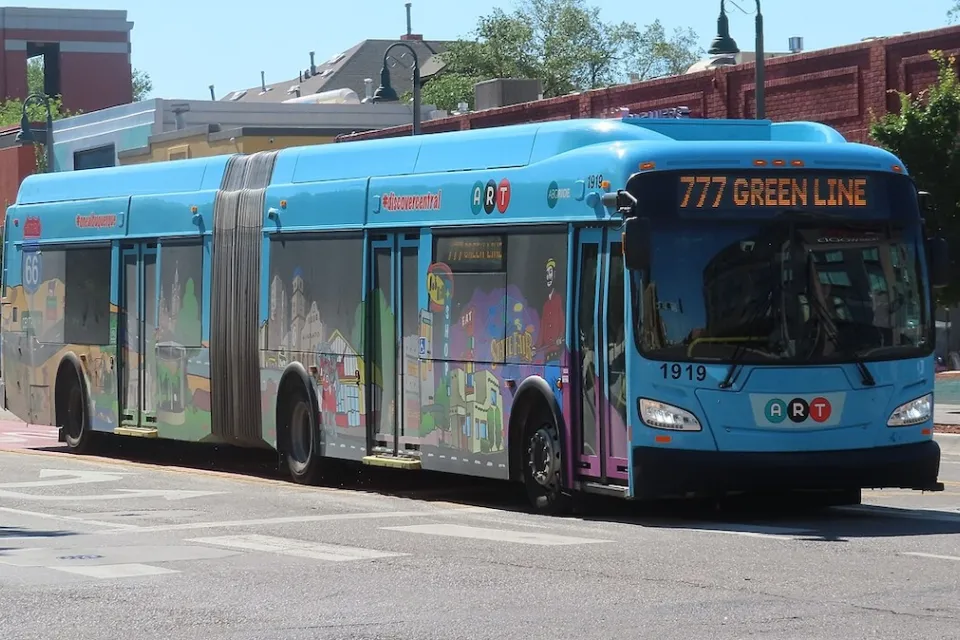 Colorful ABQ RIDE public transit bus in Albuquerque, New Mexico with low-rise brick buildings in background.